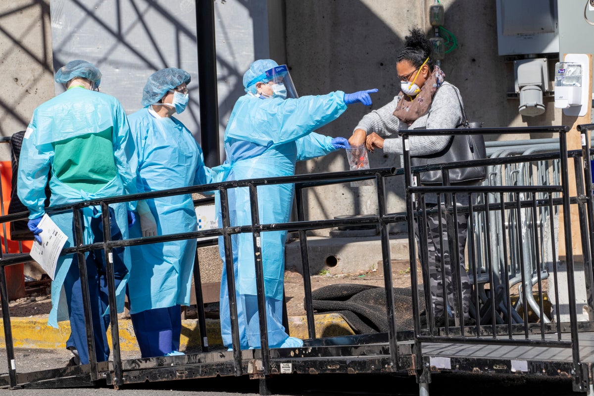 A member of the Brooklyn Hospital Center helps a person who was just tested for COVID-19 put an object in a biohazard bag, Thursday, March 26, 2020, in New York. (AP Photo/Mary Altaffer)