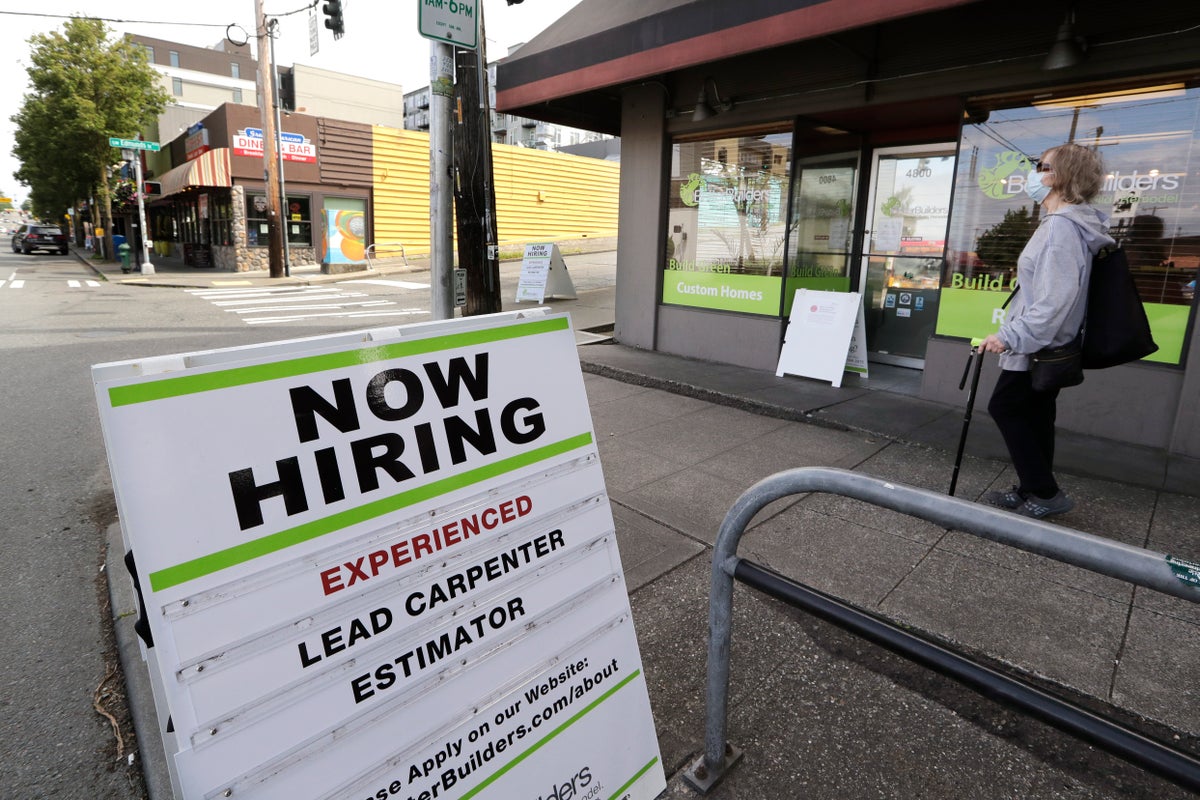 In this photo taken Thursday, June 4, 2020, a pedestrian wearing a mask walks past reader board advertising a job opening for a remodeling company, in Seattle. (AP Photo/Elaine Thompson)