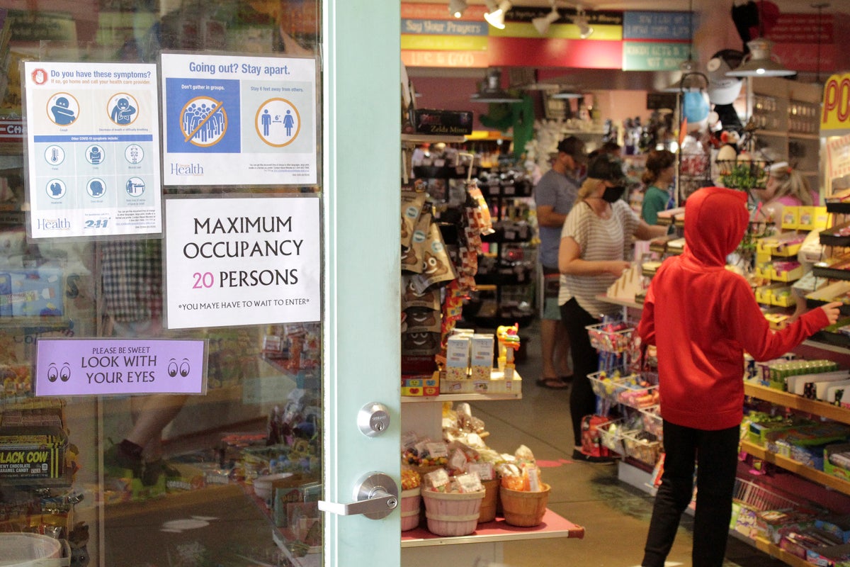 In this Thursday, May 28, 2020, photo tourists shop at Bruce's Candy Kitchen amid social distancing restrictions during the coronavirus outbreak in Cannon Beach, Ore. (AP Photo/Gillian Flaccus)