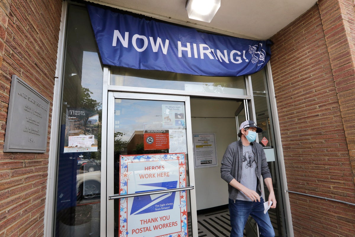In this photo taken Thursday, June 4, 2020, a customer walks out of a U.S. Post Office branch and under a banner advertising a job opening, in Seattle. The U.S. unemployment rate fell to 13.3% in May, and 2.5 million jobs were added — a surprisingly positive reading in the midst of a recession that has paralyzed the economy and depressed the job market in the wake of the viral pandemic (AP Photo/Elaine Thompson)