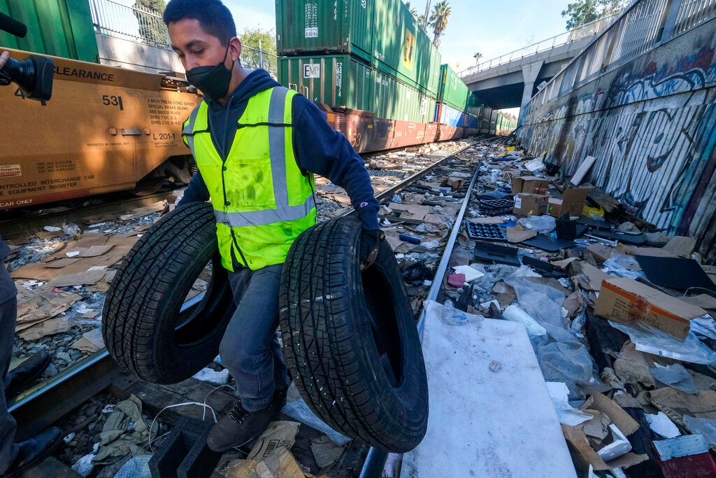 Contractor worker Luis Rosas removes vehicle tires from the shredded boxes and packages along a section of the Union Pacific train tracks in downtown Los Angeles Friday, Jan. 14, 2022. Thieves have been raiding cargo containers aboard trains nearing downtown Los Angeles for months, leaving the tracks blanketed with discarded packages. The sea of debris left behind included items that the thieves apparently didn't think were valuable enough to take, CBSLA reported Thursday. (AP Photo/Ringo H.W. Chiu)